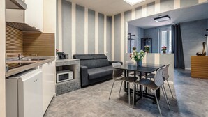A compact living space with a kitchenette, a sofa, a dining table with chairs, and a window with curtains. - Termini Jacuzzi Suite (Roma)