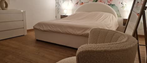 Un dormitorio con una cama, un tocador blanco, una silla redonda y un mural floral en la pared.