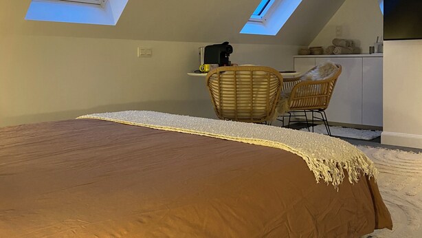 A bedroom with a large bed, a desk, two chairs, and a kitchenette.