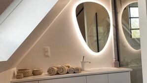 A bathroom with a white vanity, a heart-shaped mirror, and a towel rack.