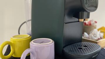 Une machine à café avec une base noire et un panneau de commande, accompagnée de deux tasses à café, une jaune et une violette, posées sur un tapis noir.