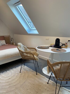 A bedroom with a skylight, a bed, a desk, and two wicker chairs.
