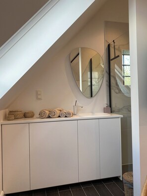 A modern bathroom with a white vanity, a large mirror, and a towel rack.