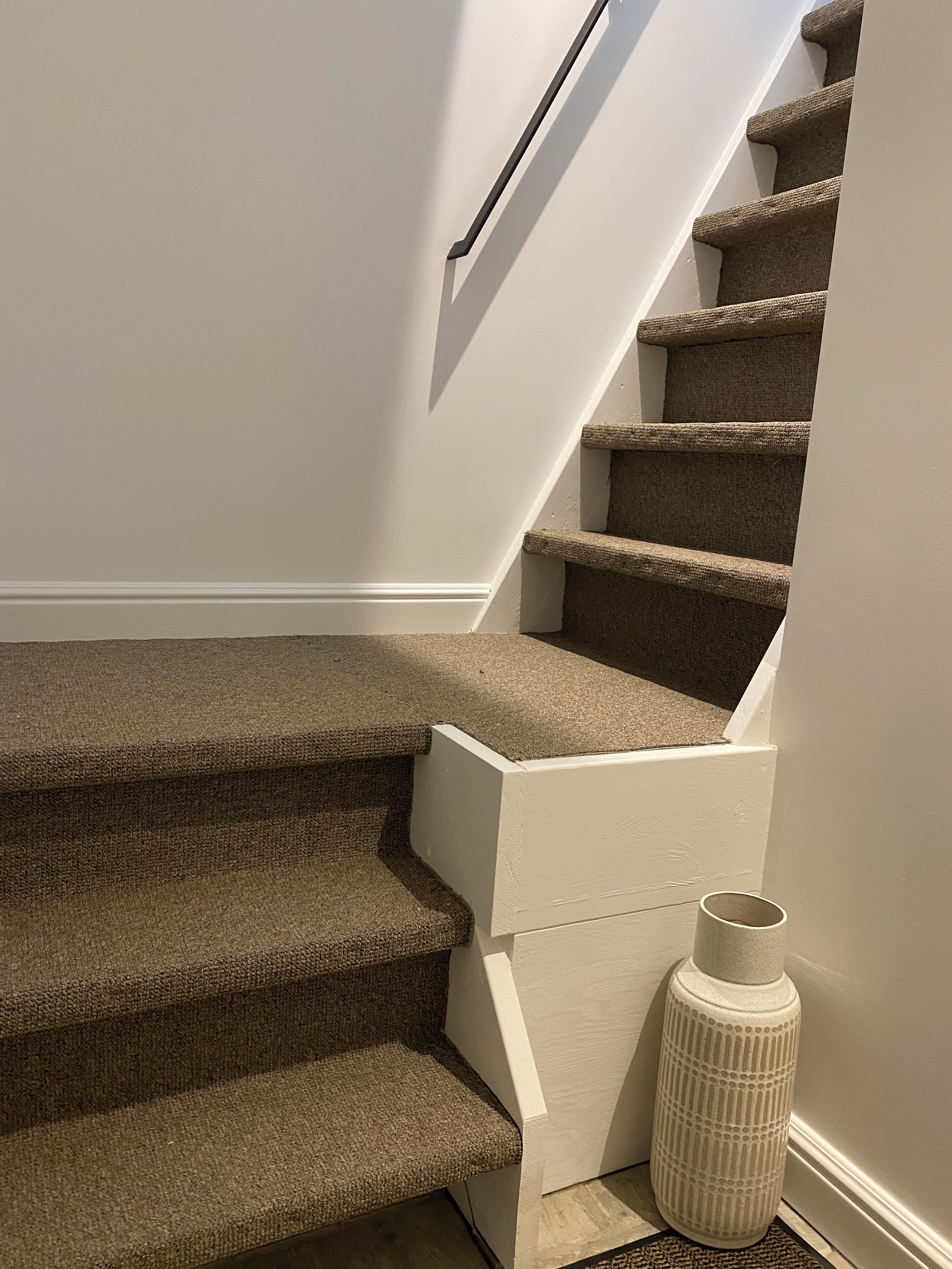 A carpeted staircase with a white wall and a white vase on the landing.