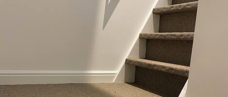 A carpeted staircase with a white wall and a white vase on the landing.