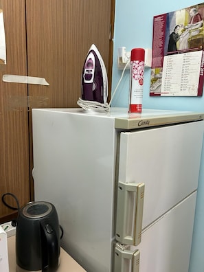 Ein kleiner Kühlschrank mit einer Mikrowelle obenauf, einem Wasserkocher und einem Kalender an der Wand.