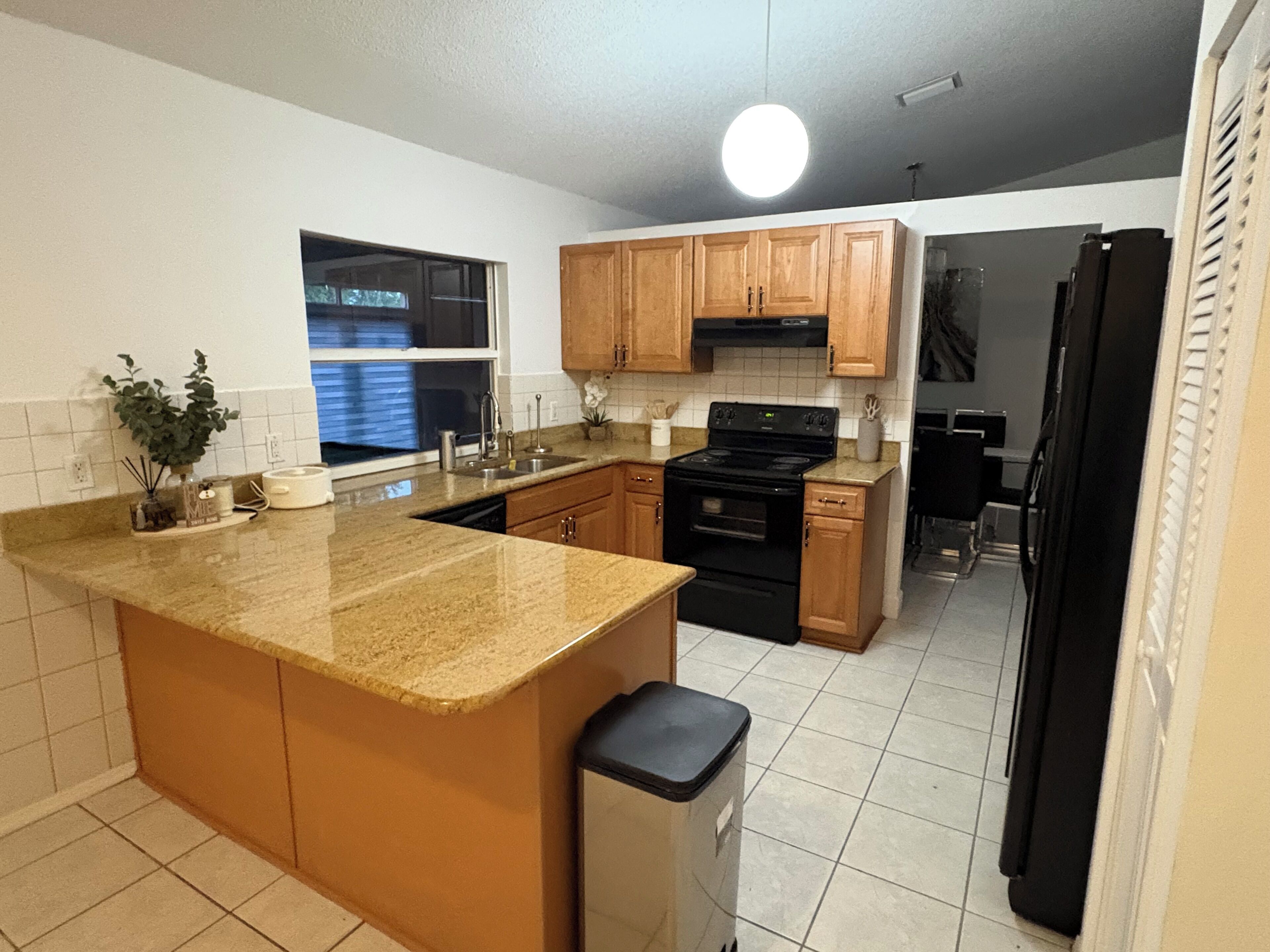 A kitchen with granite countertops, wooden cabinets, a black stove, and a trash bin.