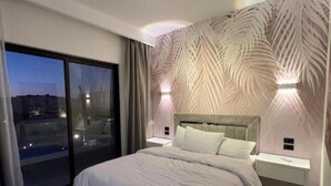 Ein modernes Schlafzimmer mit einem großen Bett, einem Nachttisch, einer Wandleuchte und Blick durch eine Schiebetür.