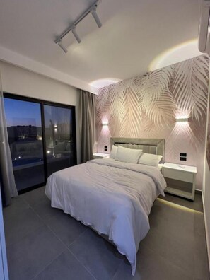 Ein modernes Schlafzimmer mit einem großen Bett, einem Nachttisch, einer Wandleuchte und Blick durch eine Schiebetür.