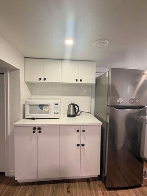 Una cocina compacta con armarios blancos, un refrigerador de acero inoxidable y un microondas.