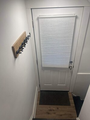 A white door with a window, a wooden coat rack, and a dark mat at the entrance. - Room to Stay in Niagara Falls (Niagara Falls)
