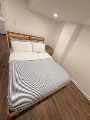 A single bed with a wooden frame and striped bedding in a room with wooden flooring and white walls. - Room to Stay in Niagara Falls (Niagara Falls)