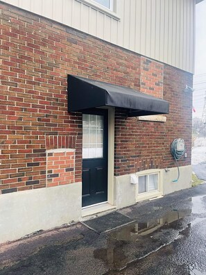A brick building with a black awning over a door, a window, and a hose connected to a wall-mounted electrical box. - Room to Stay in Niagara Falls (Niagara Falls)
