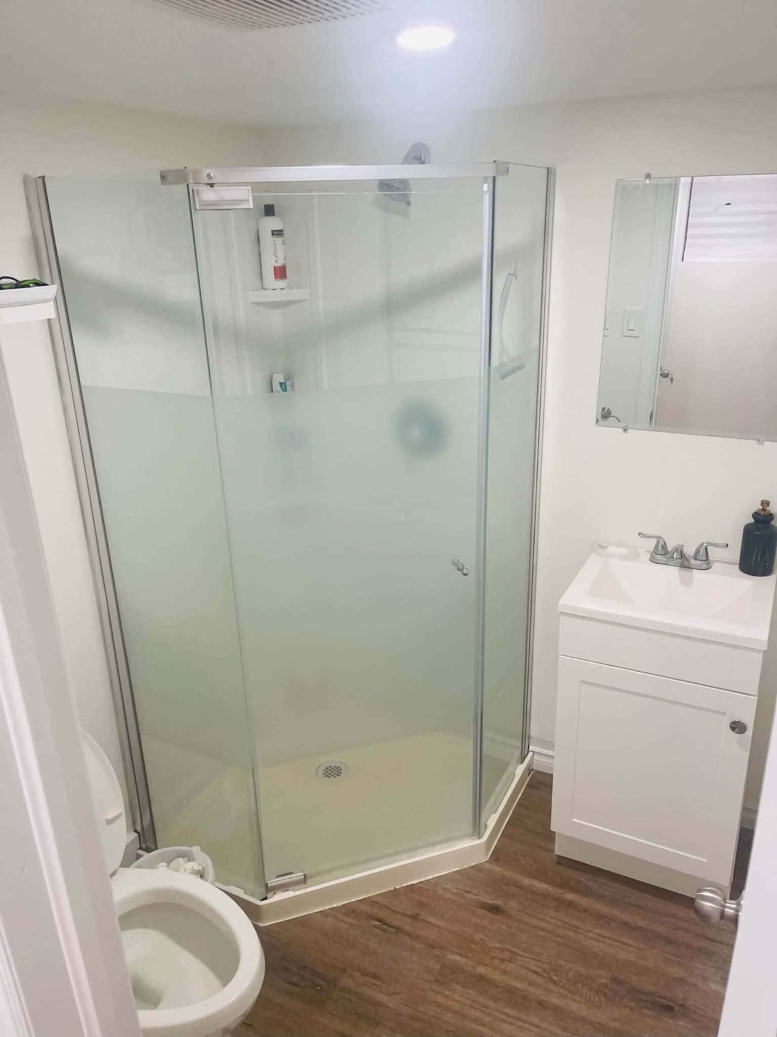 A modern bathroom with a glass-enclosed shower, a toilet, and a sink with a mirror above it.