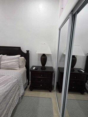 Ein Schlafzimmer mit einem Bett, einem Nachttisch mit Lampe, einem Spiegel und einem gemusterten Teppich.