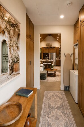 A kitchen with wooden cabinets, a refrigerator, and a dining area with a table and chairs. - Boutique Retreat • Private Sauna • 2 King Suites (West Kelowna)