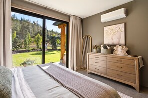 Une chambre à coucher avec un grand lit, une commode en bois, un miroir et une fenêtre donnant sur un paysage verdoyant.