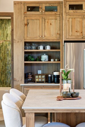 Une cuisine en bois équipée d’un réfrigérateur intégré, d’étagères pour ranger les ustensiles de cuisine et d’une table à manger avec des chaises.