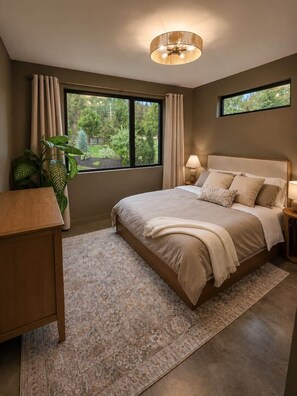 A bedroom with a large bed, bedside tables, a desk, a window with curtains, and a ceiling light fixture. - Boutique Retreat • Private Sauna • 2 King Suites (West Kelowna)