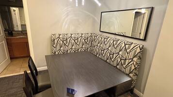 A conference room with a dark wooden table, six chairs, a patterned wall bench, a ceiling light fixture, and a wall-mounted mirror.