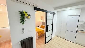 Una cocina moderna con refrigerador empotrado y una puerta corrediza que da a un dormitorio con cama y mesita de noche.