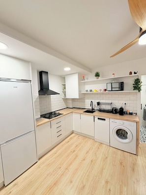 A modern kitchen with white cabinetry, a built-in stove, a microwave, and a washing machine.