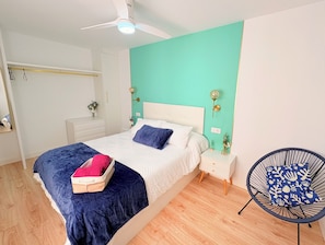 A bedroom with a bed, bedside tables, a chair, a ceiling fan, and a wall-mounted light fixture.
