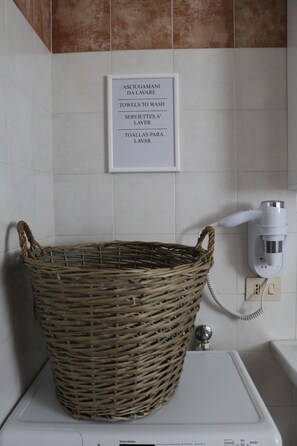 Un bany amb una paret de rajoles blanques, un cartell sobre un rentapousades blanc i una cistella de vimet, juntament amb un assecagats mans blanc.