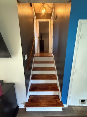 A staircase with wooden steps leading to a landing, a light fixture above, and a door on the right.