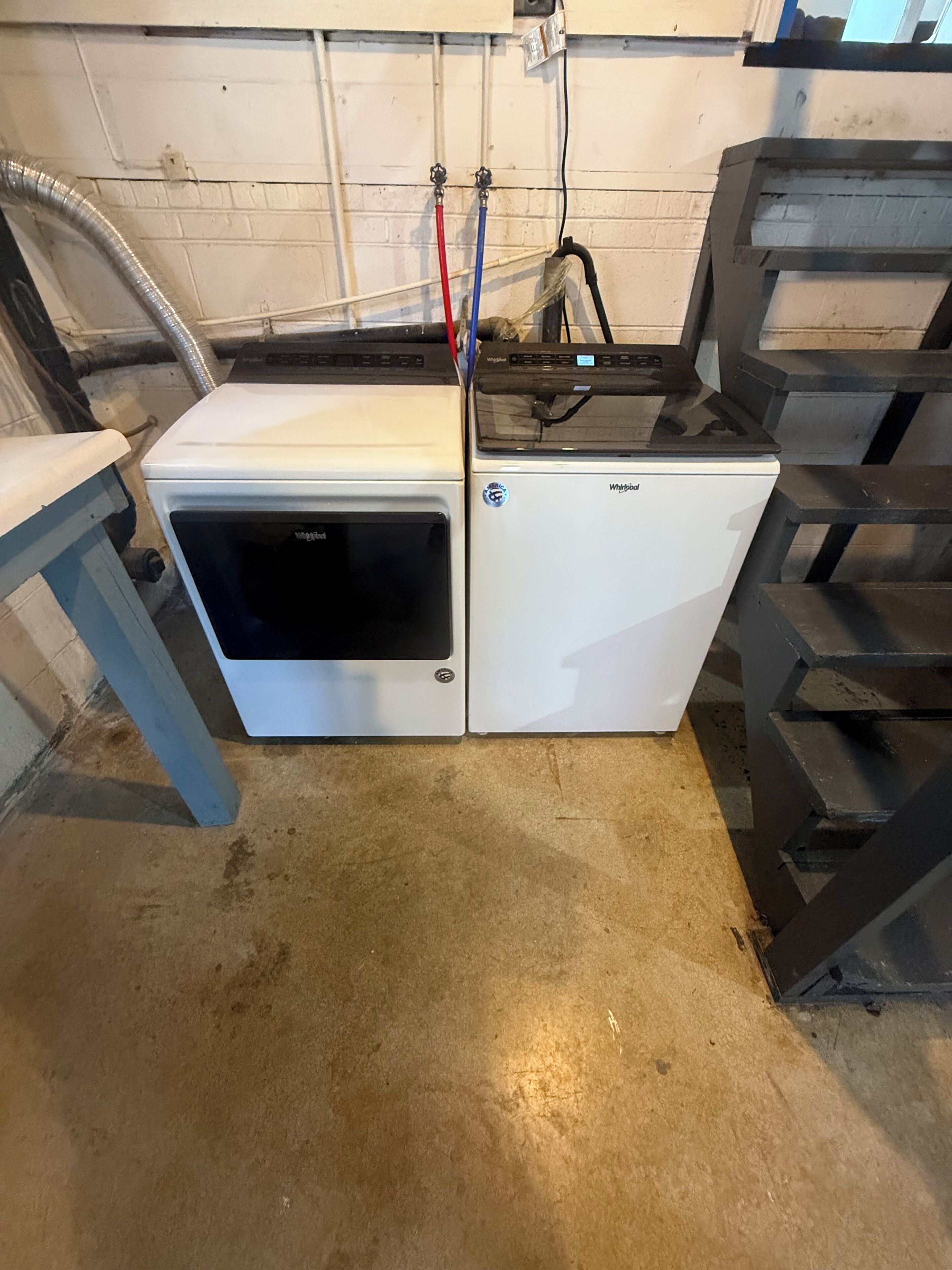 A compact, white appliance with a digital display, situated in a utilitarian space with concrete flooring and a brick wall.