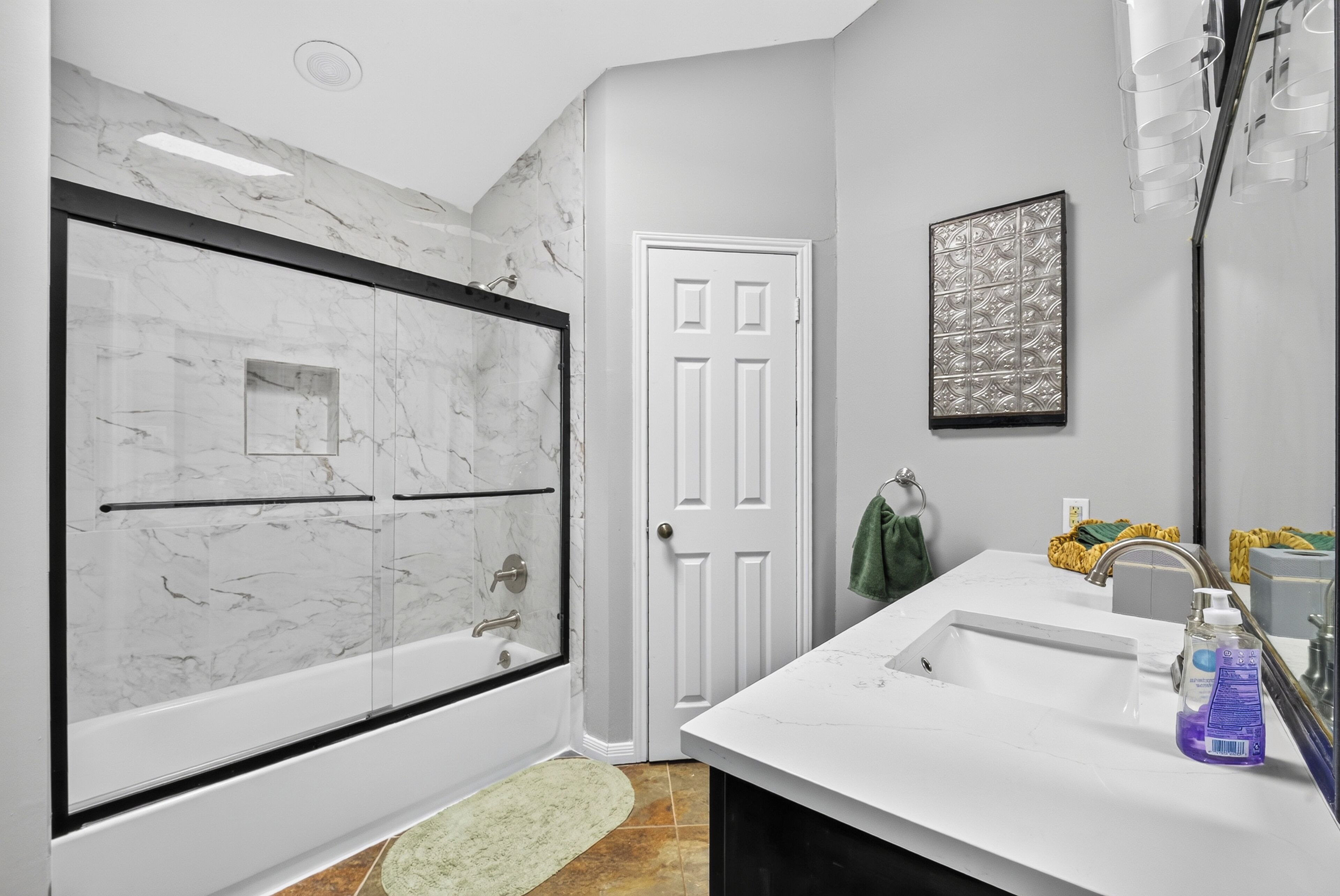 A bathroom with a marble shower enclosure, a white door, a sink with a mirror, and a towel rack.