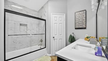 A bathroom with a marble shower enclosure, a white door, a sink with a mirror, and a towel rack.