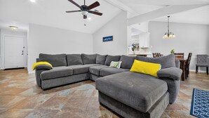 A living room with a sectional sofa, a ceiling fan, and a dining area with a chandelier.