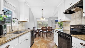 A kitchen with white cabinetry, a granite countertop, a built-in oven, and a dining area with a table and chairs.