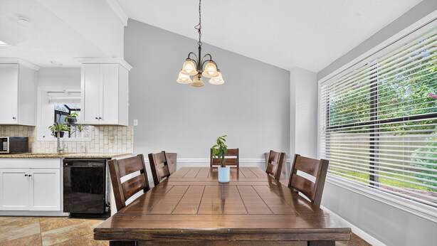 A dining area with a wooden table and chairs, a hanging light fixture, and a window with blinds.
