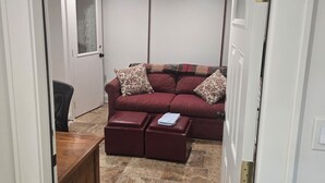 A room with a red sofa, two matching ottomans, a wooden cabinet, and a tiled floor.