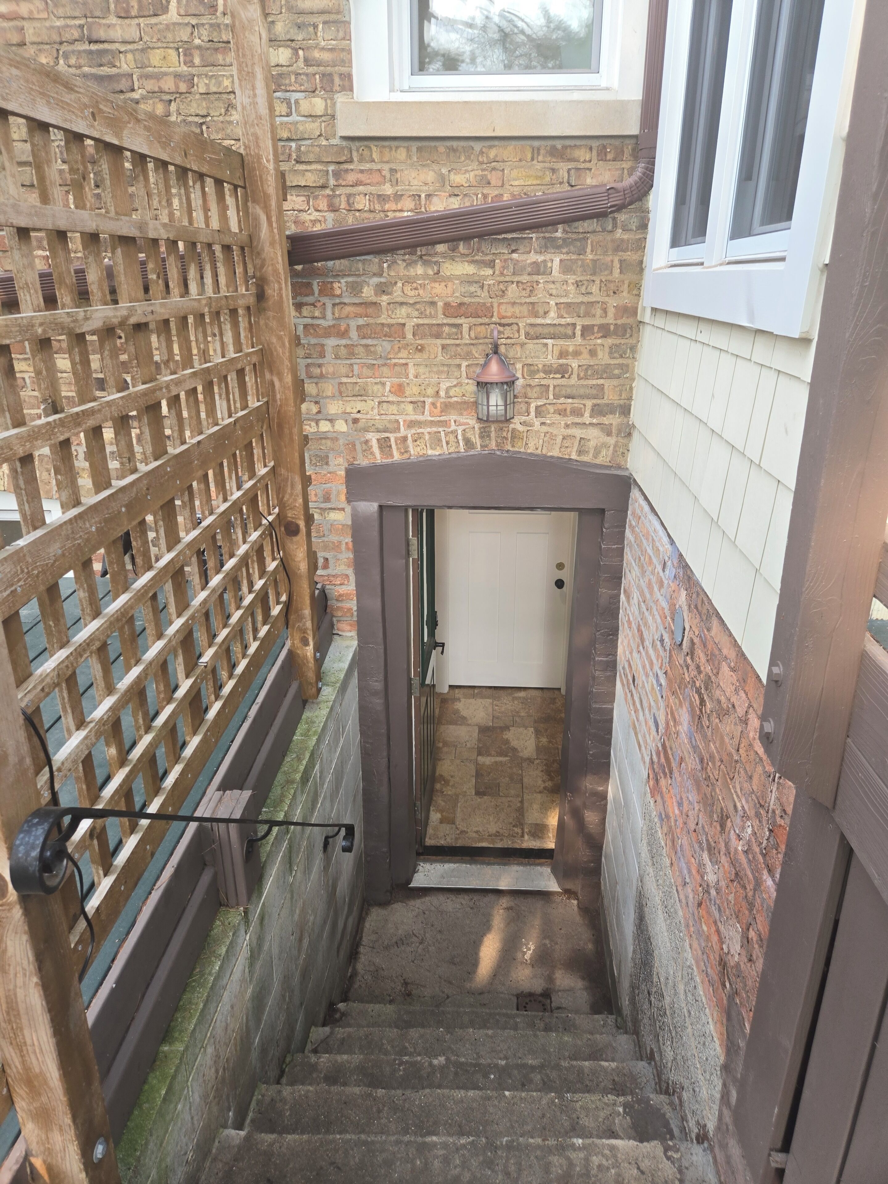 Una escalera estrecha que sube hacia una puerta con una reja metálica a la izquierda.