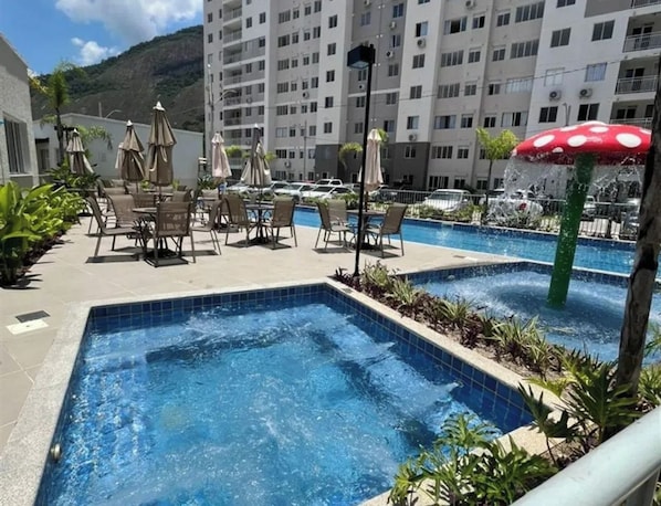 A hotel pool area with multiple swimming pools, lounge chairs, and umbrellas.