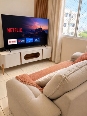Una sala de estar moderna con un televisor de pantalla plana mostrando la interfaz de Netflix, un sofá y un ventanal con vistas a edificios.