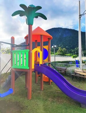 Un parque infantil con tobogán, zona de escalada y un pequeño refugio.