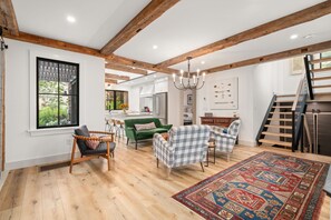 Ein geräumiges Wohnzimmer mit Holzbalken, einem grünen Sofa, karierten Sesseln und einem gemusterten Teppich.