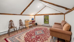 Una stanza con soffitto spiovente, un tappeto rosso decorato, un divano marrone e una scrivania con sedie.