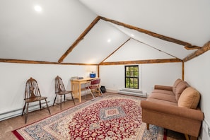 A room with a sloped ceiling, a red patterned rug, a brown sofa, and a desk with chairs. - Coastal Retreat in the Heart of Rockport: Walk to Beaches & Bearskin Neck (Rockport)