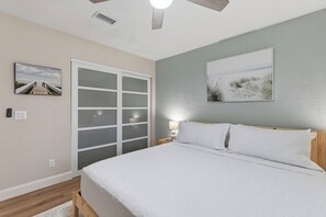 Een slaapkamer met een bed, nachtkastje, lamp, raam en deur.