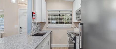 A modern kitchen with granite countertops, stainless steel appliances, and a window with blinds.