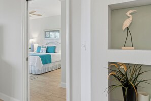 A bedroom with a bed, a bedside table, and a wall-mounted shelf with a decorative item. - 🌊 Oceanwalk 15-503 | Non-Drive Beach NSB | Soaking Tub + 2 Pools (New Smyrna Beach)