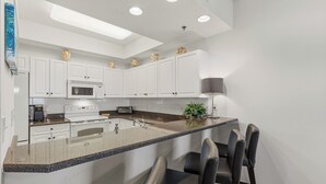 Una cocina moderna con armarios blancos, microondas integrado, estufa y pileta. Cuenta con barra desayunadora y sillas.