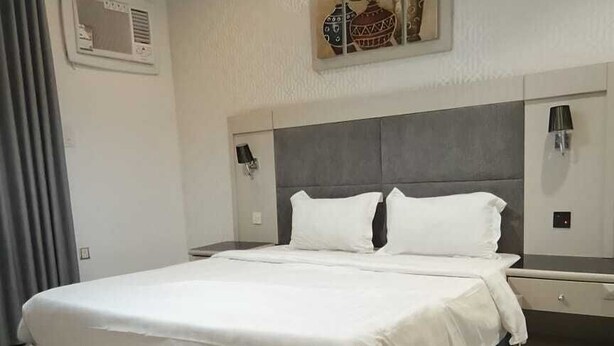 A hotel room with a large bed, a bedside table, a lamp, and a wall-mounted artwork.