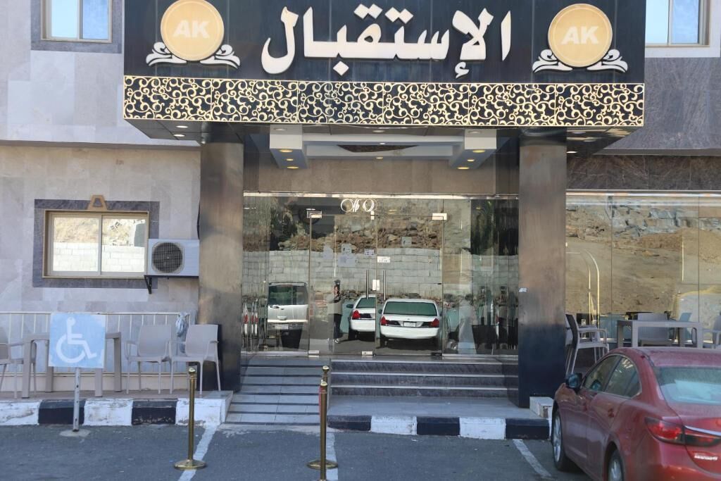 L’entrée d’un hôtel avec une façade en verre, un panneau indiquant l’accessibilité aux personnes à mobilité réduite et un espace de stationnement avec des voitures.