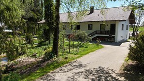 A white building with a tiled roof, a paved driveway, and a garden with trees and shrubs. - Greengarden Apartment for Construction Workers (Vilsheim)
